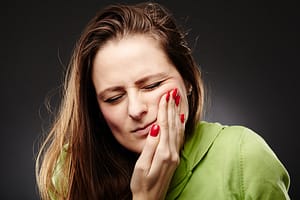Studio shot of a young woman having a severe tooth ache with hand on cheek over grey background